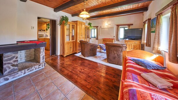 A spacious living area with a stone fireplace, wooden ceiling beams, and a cozy seating arrangement.