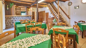 A restaurant with wooden tables and chairs, a stone wall, and a staircase.