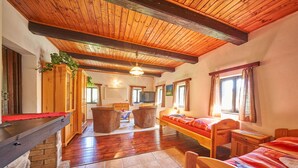 A cozy room with wooden ceilings, a fireplace, a bed, a desk, and a TV.