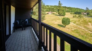 A covered porch with two chairs and a view of a grassy field with trees and a house in the distance.
