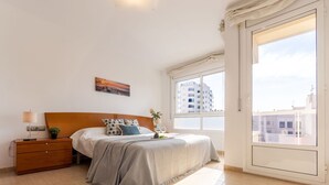 A bedroom with a bed, bedside table, lamp, and a window with a view of buildings.