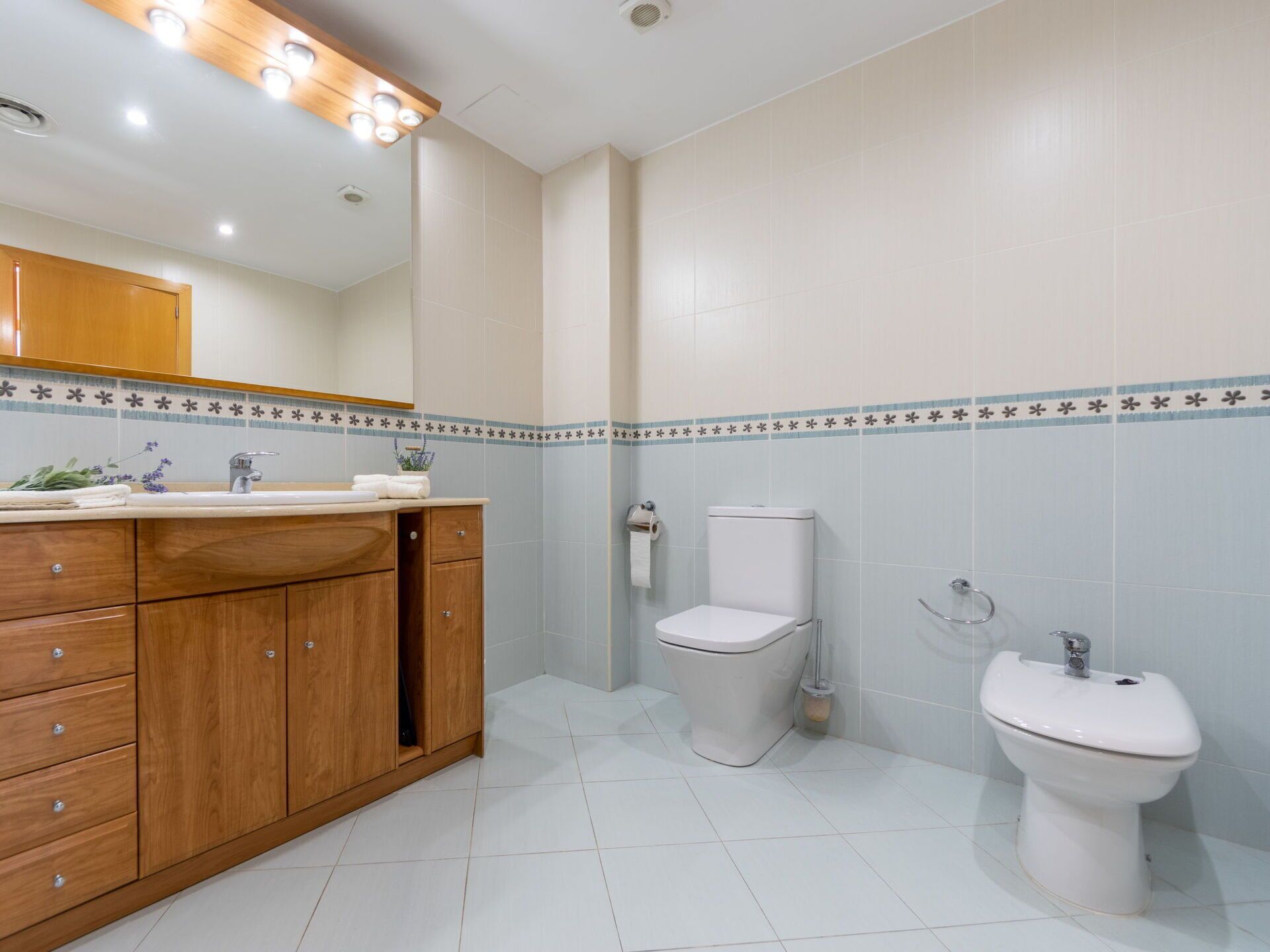A modern bathroom with a wooden vanity, a toilet, and a bidet.