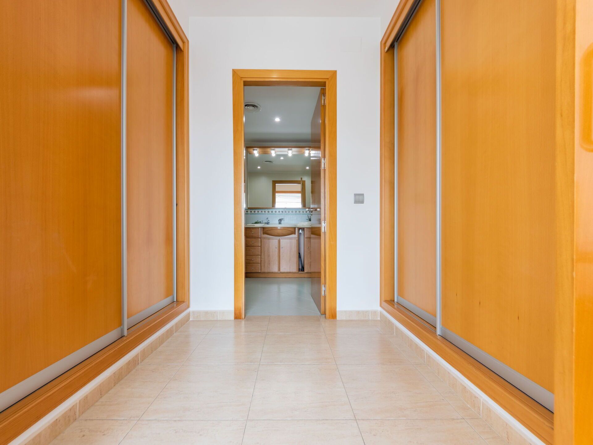 A hallway leading to a bathroom with wooden doors and a tiled floor.
