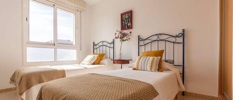 Un dormitorio con dos camas, una ventana con persianas, una mesita de noche con un florero y un reloj de pared.