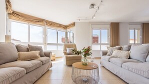 A spacious living room with two sofas, a coffee table, and a chair. Large windows provide ample natural light.
