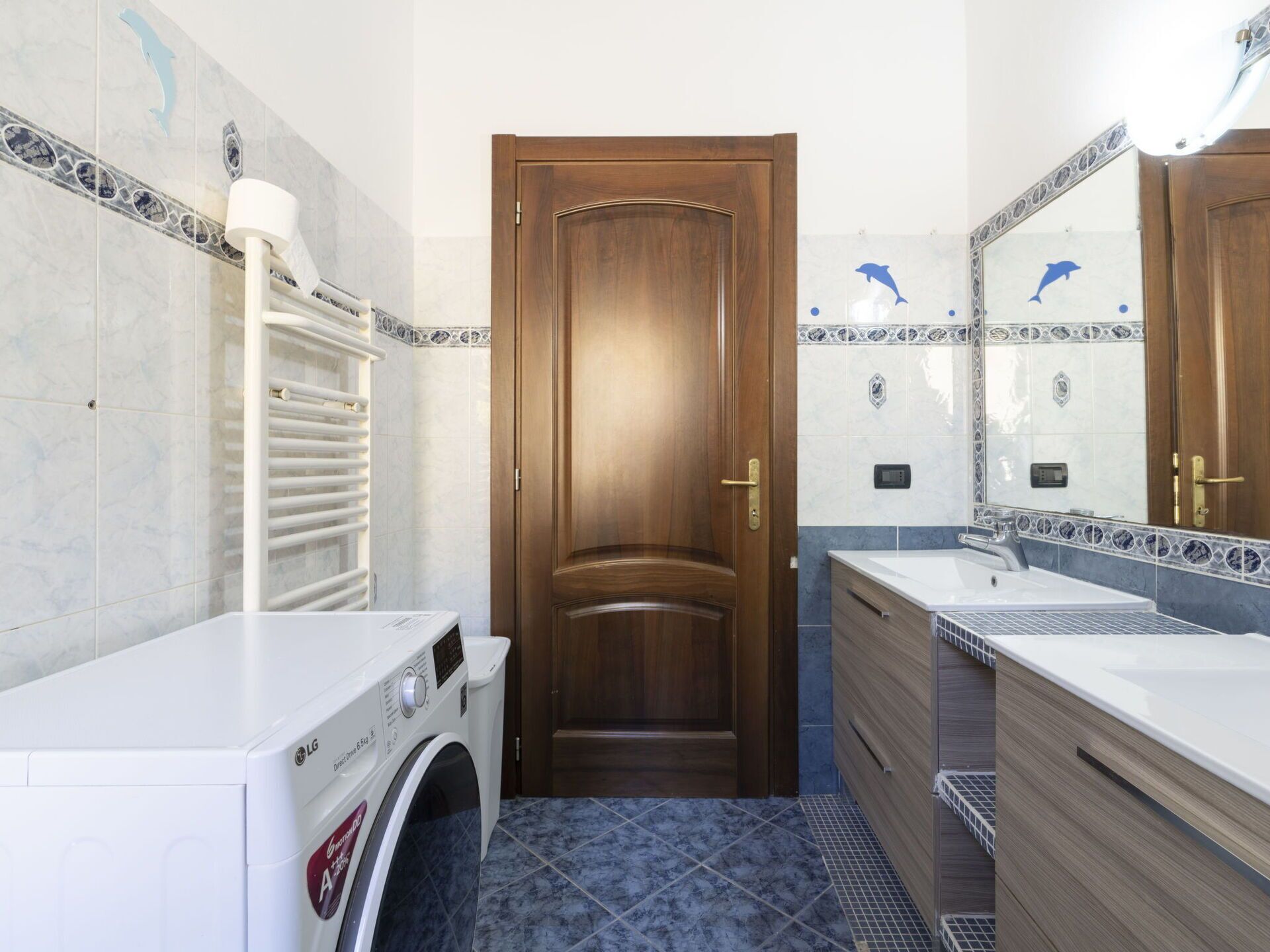 A bathroom with a wooden door, a washing machine, a sink, and a mirror.