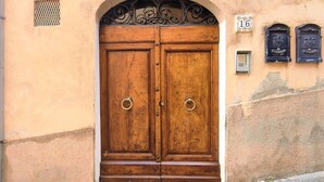 Une porte à deux battants en bois, dotée d’une poignée en forme d’anneau métallique, encadrée par un arc en plein cintre et surmontée d’éléments décoratifs en métal.