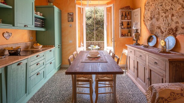 Une cuisine chaleureuse avec une table et des chaises en bois, des armoires vertes et une vue sur l’extérieur.