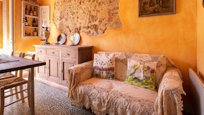 Una habitación acogedora con una mesa de madera, un sofá estampado y un tapiz colgado en la pared.
