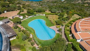 Ett flygbildsbild av en fastighet vid kusten med en stor swimmingpool, radhus och utsikt över havet och bergen.