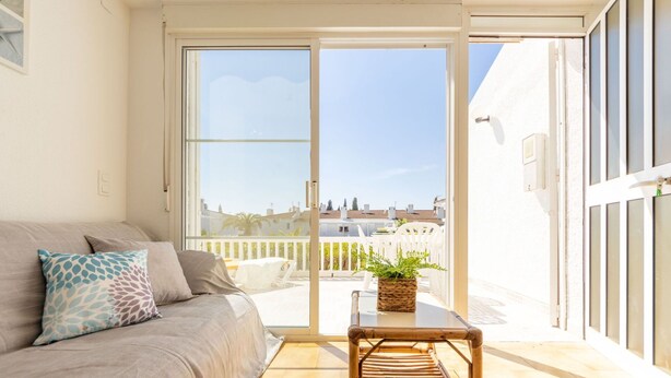 A balcony with a wicker chair, a potted plant, and a view of a cityscape.