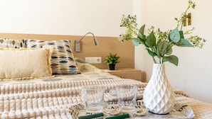 A neatly made bed with patterned pillows, a bedside table with a lamp, a small potted plant, and a vase with flowers on a tray.