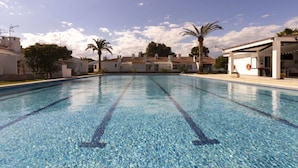 A swimming pool with clear blue water, surrounded by white buildings with palm trees.