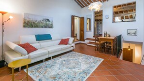Un salon chaleureux avec un canapé blanc, un tapis à motifs et un coin repas comprenant une table et des chaises en bois.