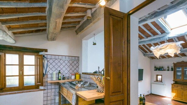 Une cuisine rustique avec des poutres apparentes, une table en bois et un mur recouvert de carreaux.