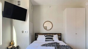 Un dormitorio con una cama, televisión montada en la pared, un espejo redondo y un armario.