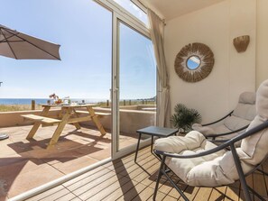 Een balkon met een houten tafel en stoelen, een grote parasol en uitzicht op zee.