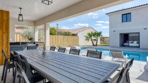 An outdoor dining area with a wooden table and chairs, a pool, and a modern building in the background. - Stunning private villa for 10 guests with A/C, private pool, WIFI, TV, terrace and pets allowed (Lanton)