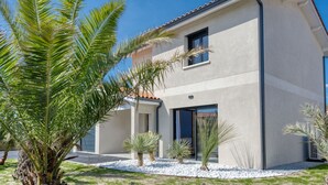 A modern two-story house with a flat roof, large windows, and a well-maintained garden with palm trees and a gravel pathway. - Stunning private villa for 10 guests with A/C, private pool, WIFI, TV, terrace and pets allowed (Lanton)
