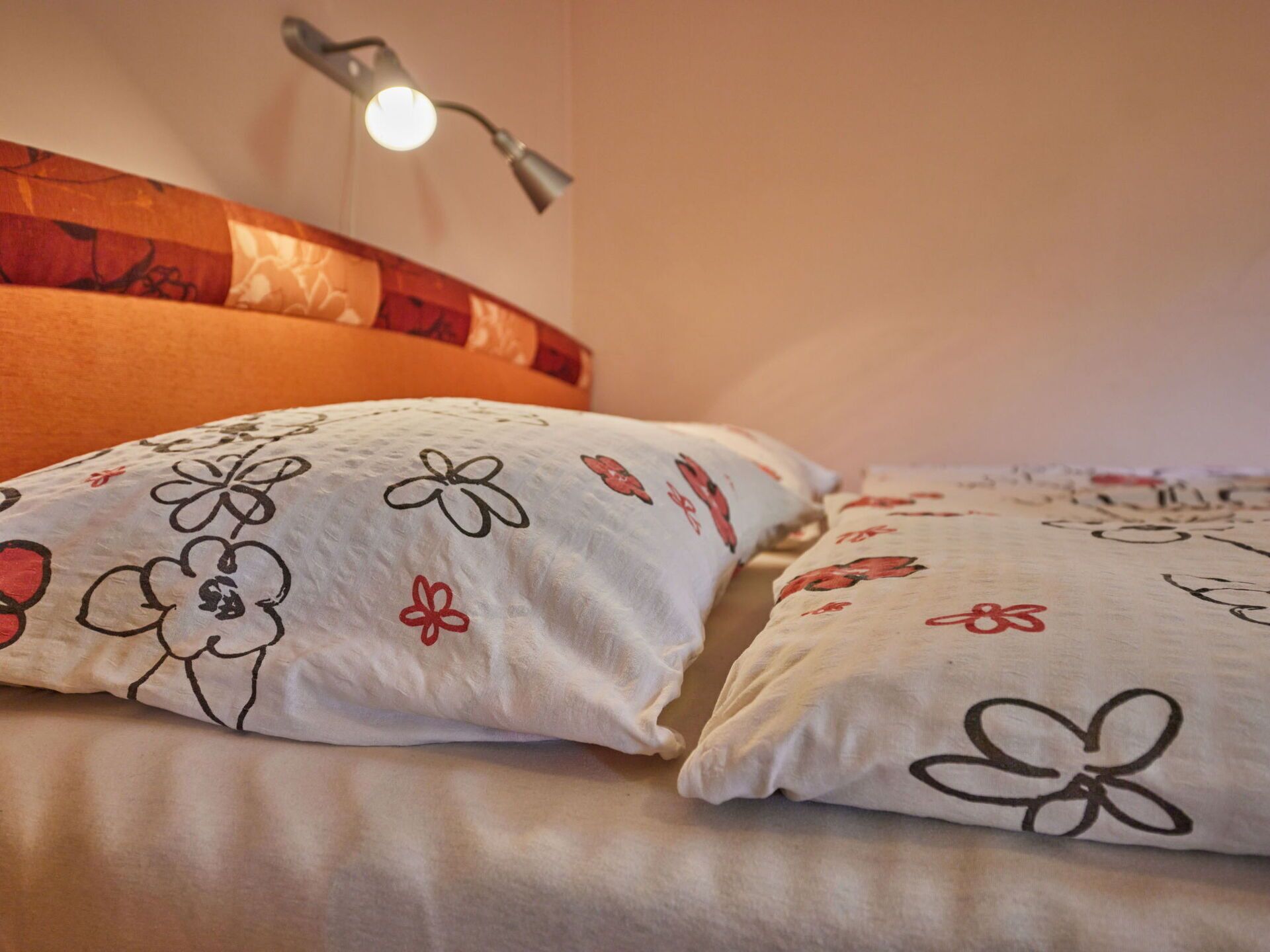 A bed with white pillows featuring floral patterns and a red headboard.