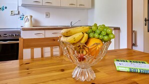 A kitchen with white cabinets, a wooden table, and a fruit bowl containing bananas, grapes, an apple, and an orange. - Nice apartment for 4 people with WIFI, TV, patio and pets allowed (Dvur Králové Nad Labem)