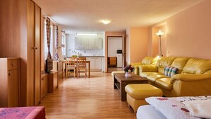 A compact living space with a kitchenette, a yellow sofa, a wooden dining table, and a bed with a floral bedspread. - Nice apartment for 4 people with WIFI, TV, patio and pets allowed (Dvur Králové Nad Labem)