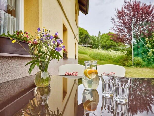 A glass table with a vase of flowers, a pitcher, and two Coca-Cola glasses.