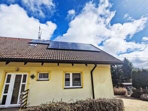 A yellow house with a tiled roof, solar panels, and a small garden.