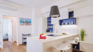 Cozinha moderna com armários brancos, uma ilha central com banquetas e uma luminária pendente.