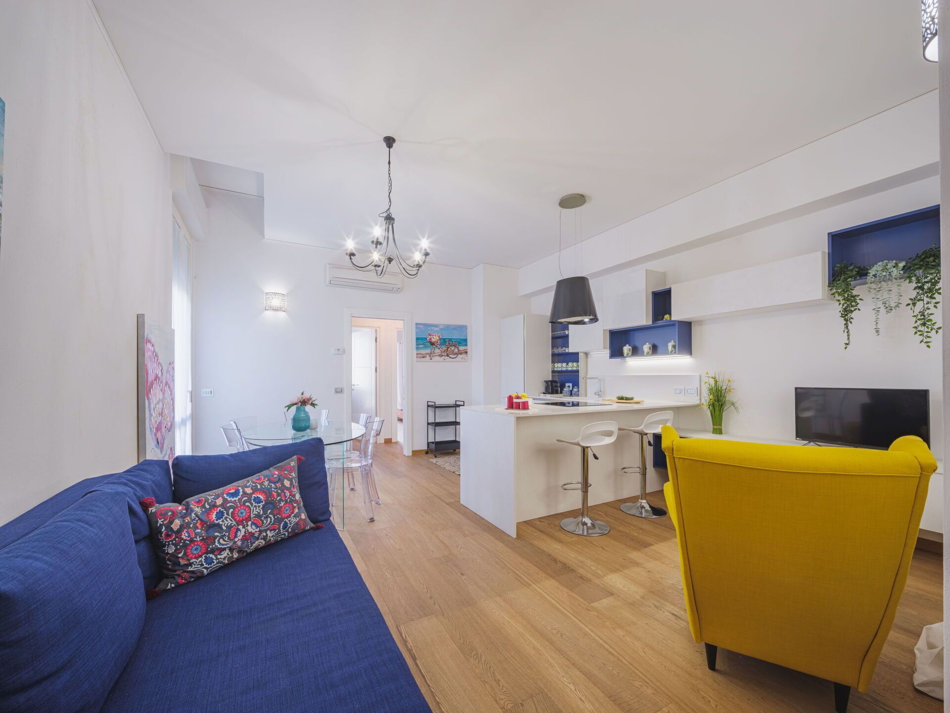 A modern living room with a blue sofa, yellow armchair, and a dining area with a glass table.