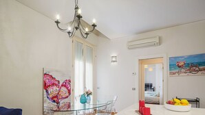 Uma sala de jantar moderna com uma mesa e cadeiras de vidro, um candelabro e obras de arte nas paredes.