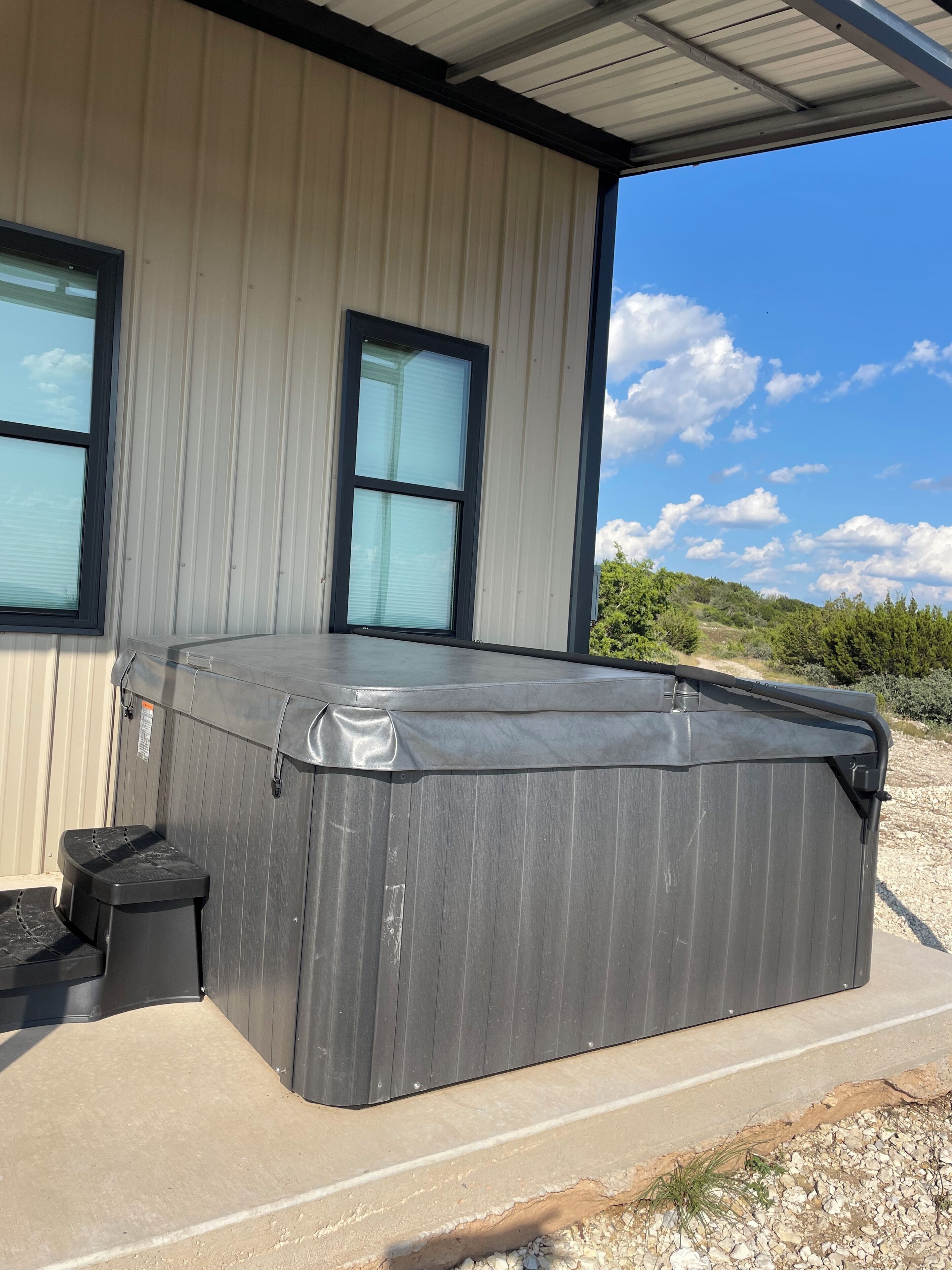 A hot tub next to a building with large windows and a clear sky.