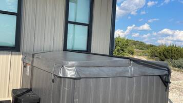 A hot tub next to a building with large windows and a clear sky.