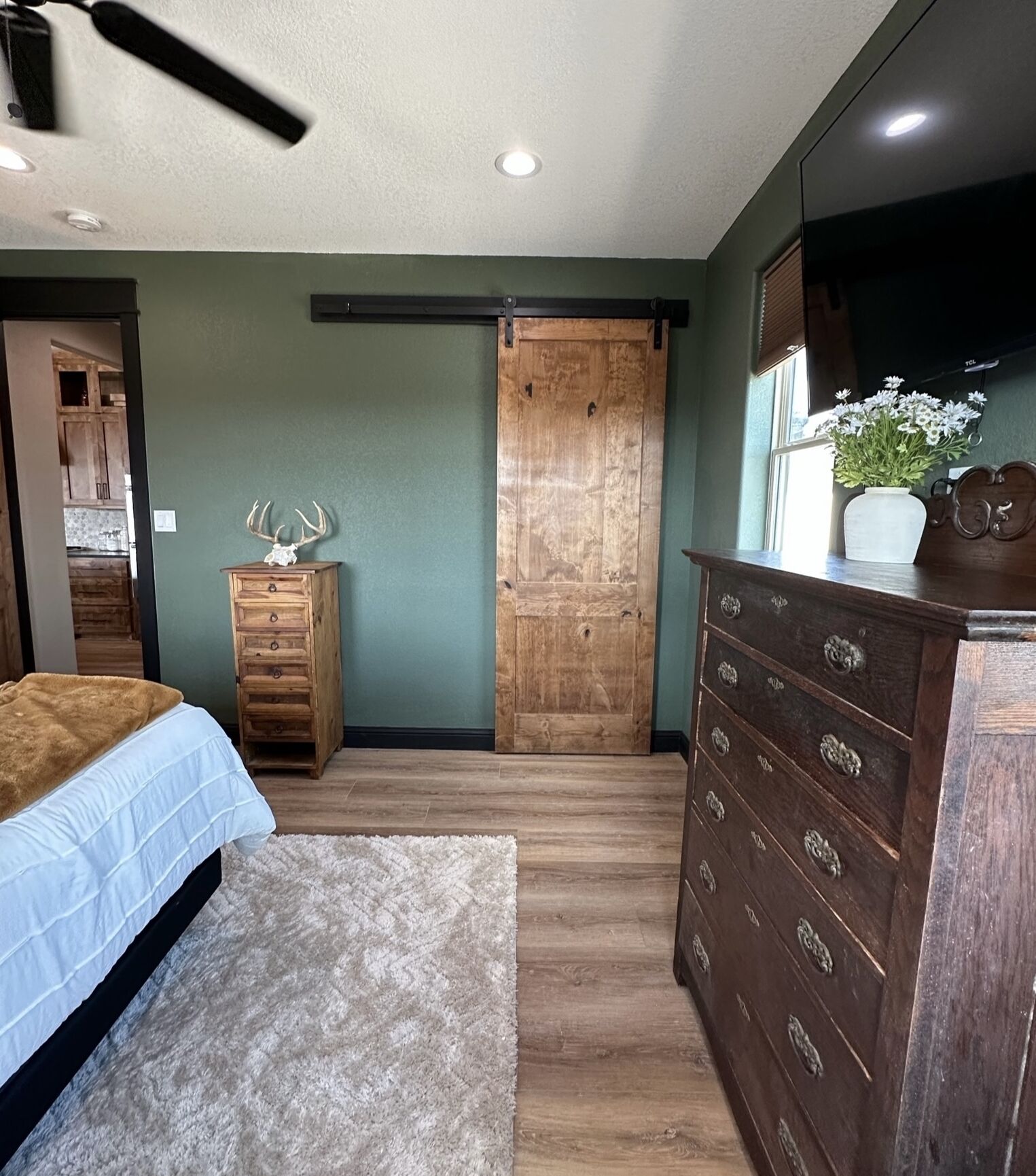 Un dormitorio con cama, cómoda, puerta de madera y ventana con planta.