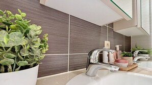 Ein modernes Badezimmer mit einem weißen Waschbecken, einem Chrom-Wasserhahn und einer Topfpflanze.