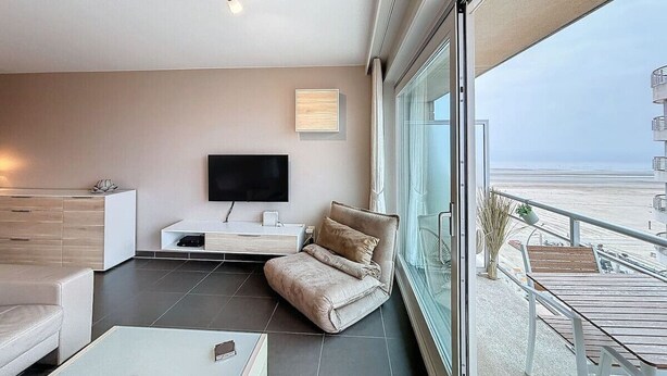 Ein modernes Wohnzimmer mit Flachbildfernseher, einer Couch, einem Couchtisch und einem Balkon mit Blick auf den Strand.