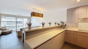Eine moderne Küche mit einer zentralen Kochinsel, Holzschränken und Blick auf die Stadt durch große Fenster.