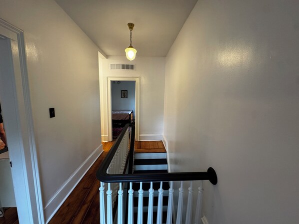A staircase with white balusters and a black handrail leading to a bedroom with a bed and a window.