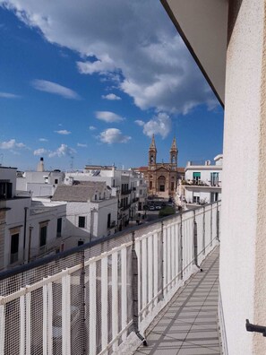 Parveke, josta avautuu näkymä historialliseen, kahden tornin omaavaan kirkkoon, kirkkaan siniselle taivaalle ja jalankulkijoiden käytävälle.