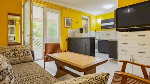 Un espacio habitable compacto con sofá, mesa de comedor y zona de cocina con armarios y televisor.