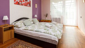 Un dormitorio con cama, mesita de noche, lámpara, ventana con cortinas y un cuadro en la pared.