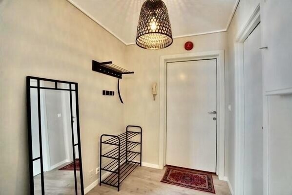A hallway with a mirror, a metal rack, a door, and a hanging light fixture.