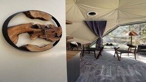 Un interior moderno con una obra de arte de madera en la pared, una zona de comedor con mesa y sillas, y un ventanal con vistas a la vegetación.