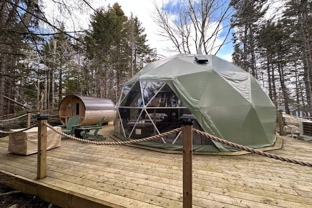 Una tenda a cupola geodetica con un pontile in legno, circondata da alberi.