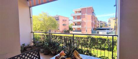 Un balcon avec une table dressée pour un repas, des plantes en pot et une vue sur des immeubles d’habitation.