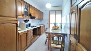 A kitchen with wooden cabinets, a microwave, a sink, and a dining table with chairs. - Nice apartment for 3 people with WIFI, TV, terrace and pets allowed (Follonica)