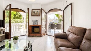 A spacious living room with a leather sofa, a glass coffee table, and a fireplace. There is a balcony with outdoor furniture and a view of greenery. - Stunning private villa for 6 people with WIFI, TV, terrace and pets allowed (Empuriabrava)