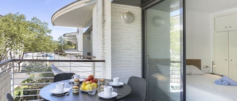 A modern balcony with a dining table set for two, featuring a fruit bowl and cups.