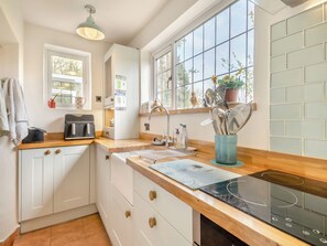 A kitchen with white cabinets, a wooden countertop, a built-in stove, and a window with a view of trees.