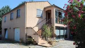Ein zweistöckiges Haus mit Steinstufen, einem Balkon und einem Garten mit rosa Blumen.